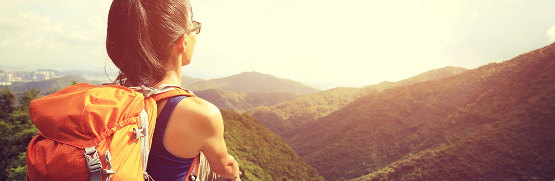 Woman with backpack sitting on rock looking out over trees and mountain range