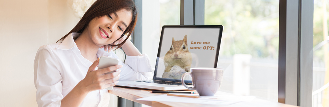 Woman sitting at table with smart phone in hand, laptop with a squirrel on it and a cup of coffee