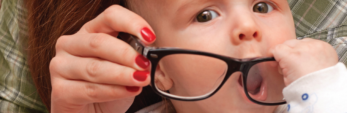 Picture of a baby with a pair of eyeglasses and trying to eat them