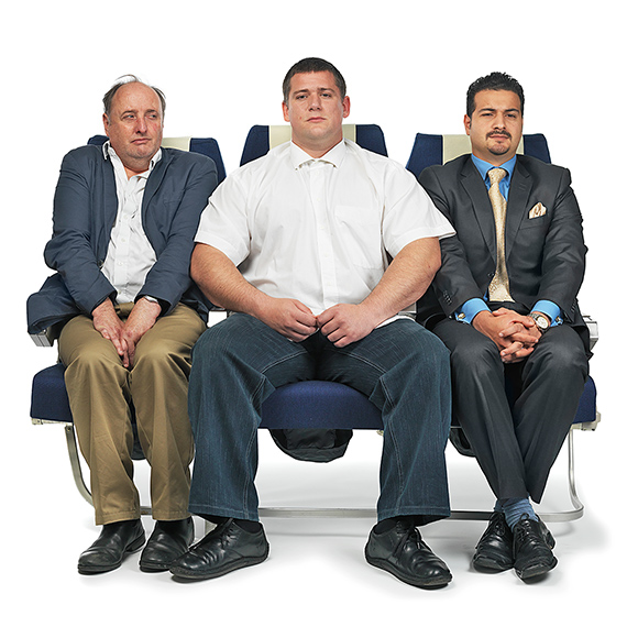 Picture of 3 people jammed into their seats in coach class on an airplane