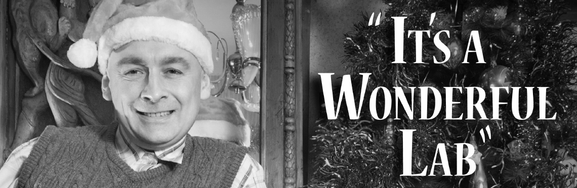 Vintage black and white picture of a man with a santa hat standing next to a christmas tree with the text, 'It's a Wonderful Lab'.